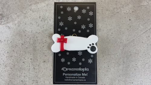 Ornament of dog bone with ribbon and paw print,shown on backing card and decorated Christmas tree.