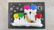 Family ornament with 5 white snowmen in bright hats, holding a hockey stick, shown on backing card and Christmas tree.
