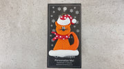 Ornament of orange cat in red and white polka dot Christmas hat and scarf, shown on backing card and Christmas tree.