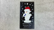 Ornament of white snowman in red hat holding a white badminton birdie, shown on backing card and Christmas tree.