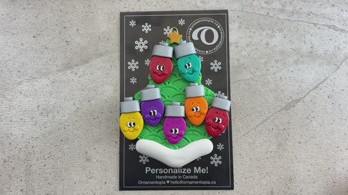 Christmas tree ornament decorated with 7 light bulbs with smiling faces, shown on  backing card and decorated Christmas tree.