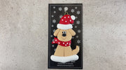 Ornament of tan dog in a red and white polka dot Christmas hat and scarf, shown on backing card and Christmas tree.