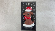 Ornament of brown dog in a red and white polka dot Christmas hat and scarf, shown on backing card and Christmas tree.