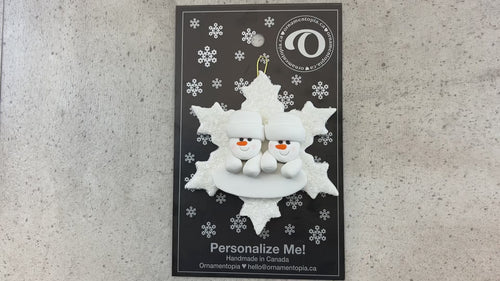 Family ornament with 2 white snowmen stacked on top of a glitter white snowflake, shown on backing card and Christmas tree.