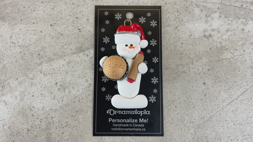 Ornament of white snowman in red hat holding a baked pie and rolling pin, shown on backing card and Christmas tree.