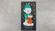 Ornament of snowman in a green shirt and hat with orange cat in Christmas hat, shown on backing card and Christmas tree.