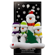 Family ornament with 1 large and 3 small white snowmen in bright scarves, with green Christmas tree, on display backing card.