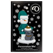 Ornament of snowman in a green shirt and hat with grey cat in Christmas hat, on display backing card.
