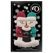 Ornament of snowman couple in red and green shirts and hats with a black cat in Christmas hat, on a display backing card.