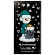 Ornament of snowman in green shirt and hat with grey dog in Christmas hat, on display backing card.