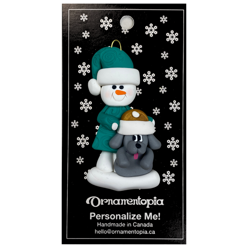 Ornament of snowman in green shirt and hat with grey dog in Christmas hat, on display backing card.