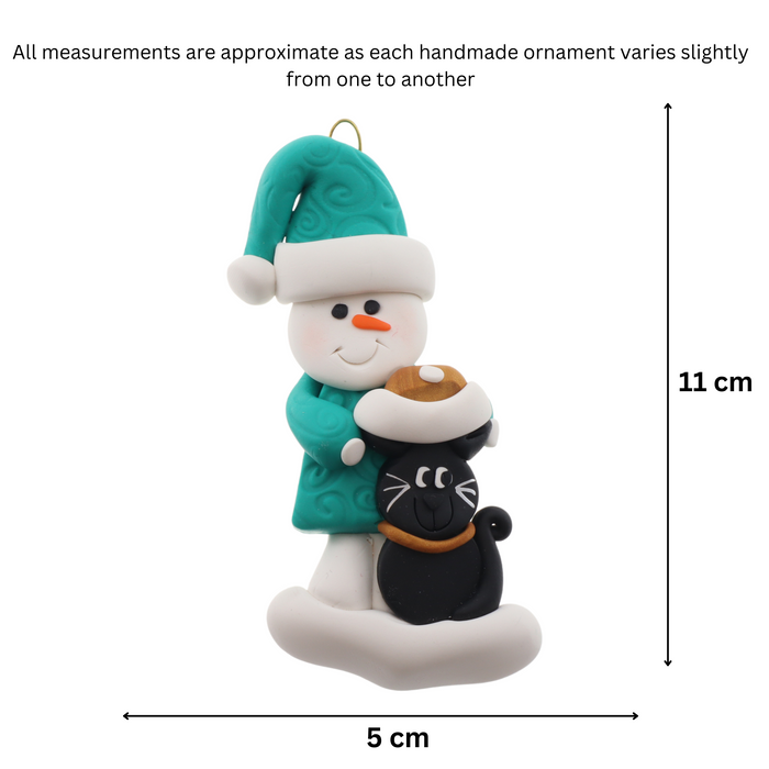 Ornament of snowman in a green shirt and hat with black cat in Christmas hat, graphed to show size (5x11cm).